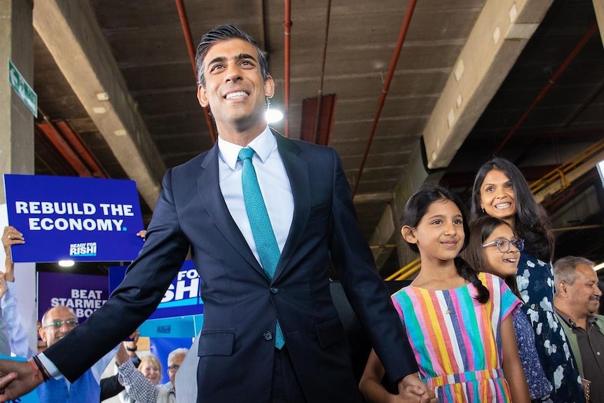 Rishi Sunak smiling while holding a little girl's hand 