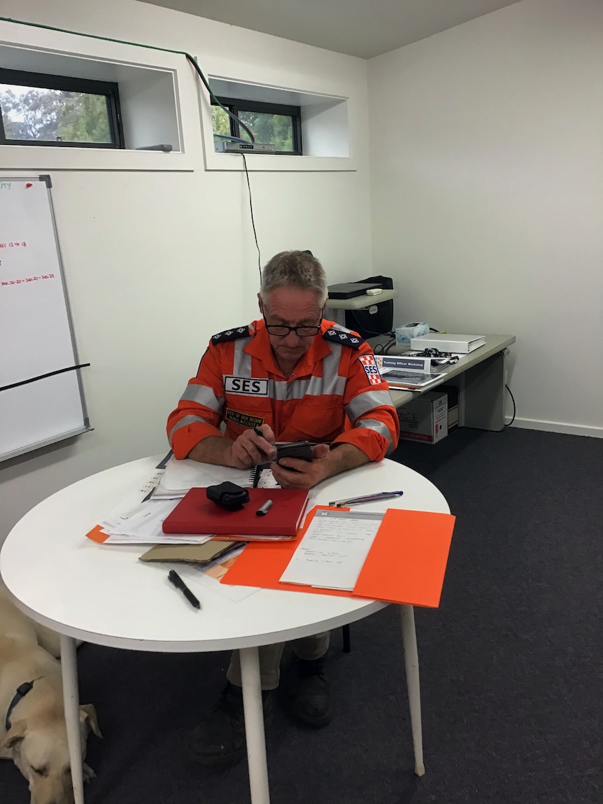 An older man wearing an SES uniform sitting in an office on his phone
