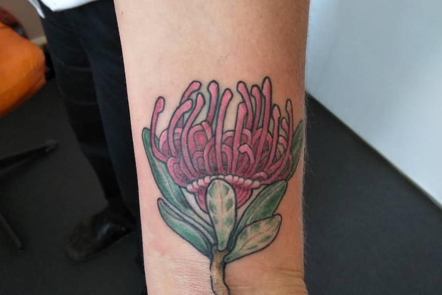A red flower with green foliage tattooed on a wrist