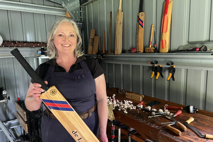 A woman smiles as she holds up a cricket bat.