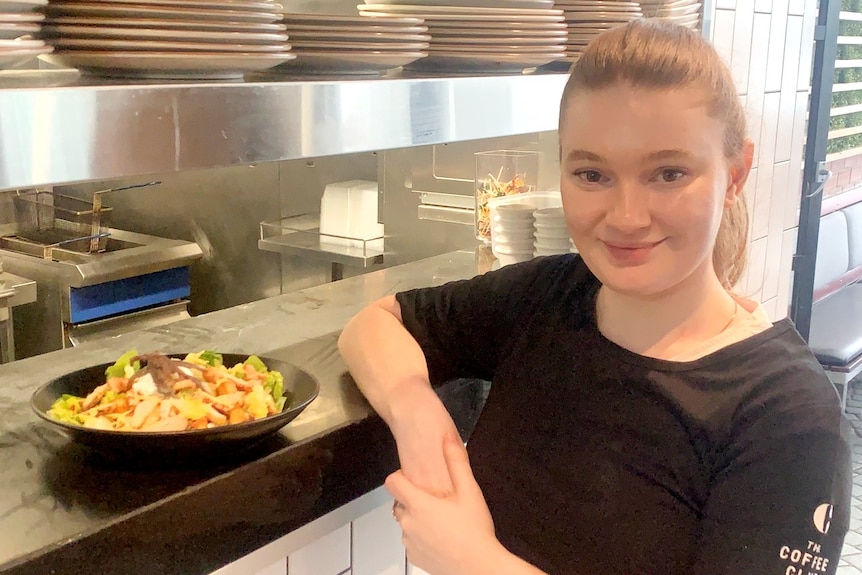 Teegan Josselyn smiles and leans on a restaurant kitchen counter, on which rests a meal with some eggs.