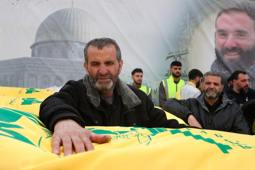 Ahmad Bazzi, the father of Australian Hezbollah fighter Ali Bazzi, places his hand on coffin draped in yellow and green fabric 