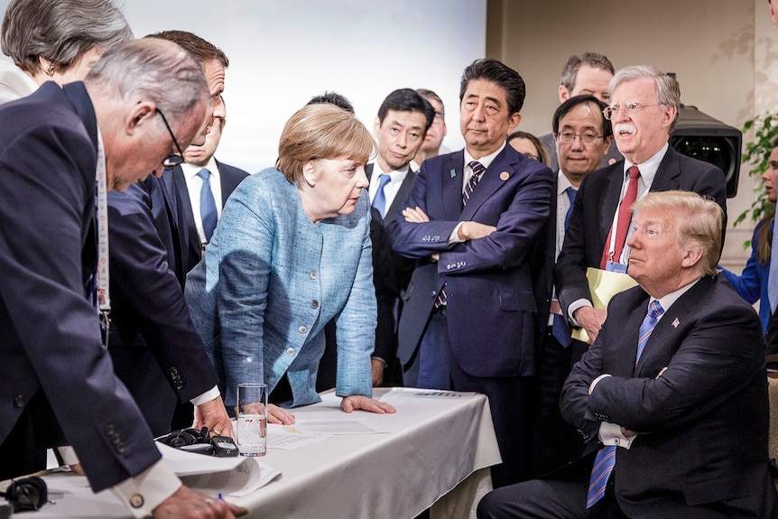 World leaders surround Doland Trump as he sits down, John Bolton by his side