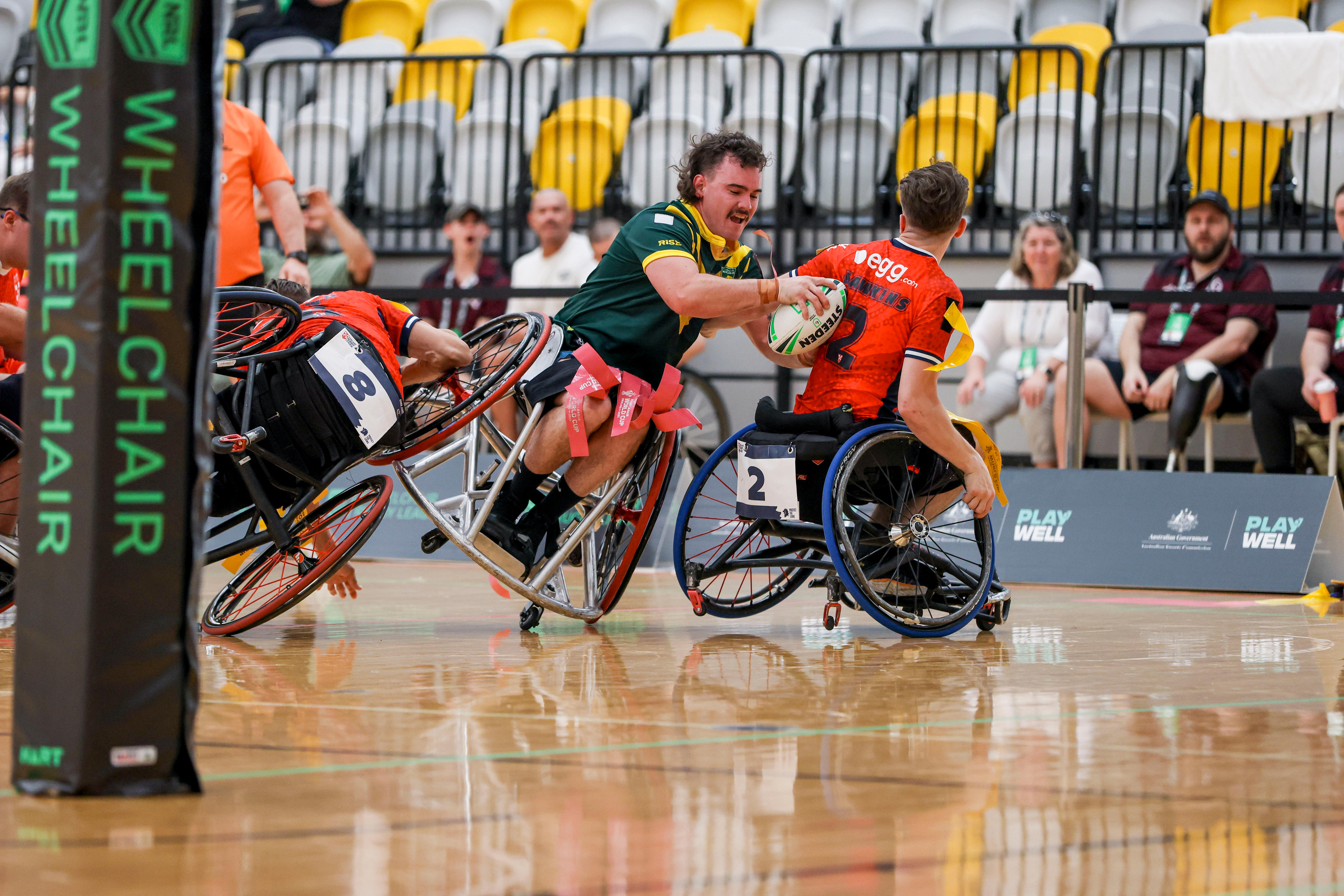 A wheelchair rugby league player in green dives to score a try while a player in red attempts a tackle