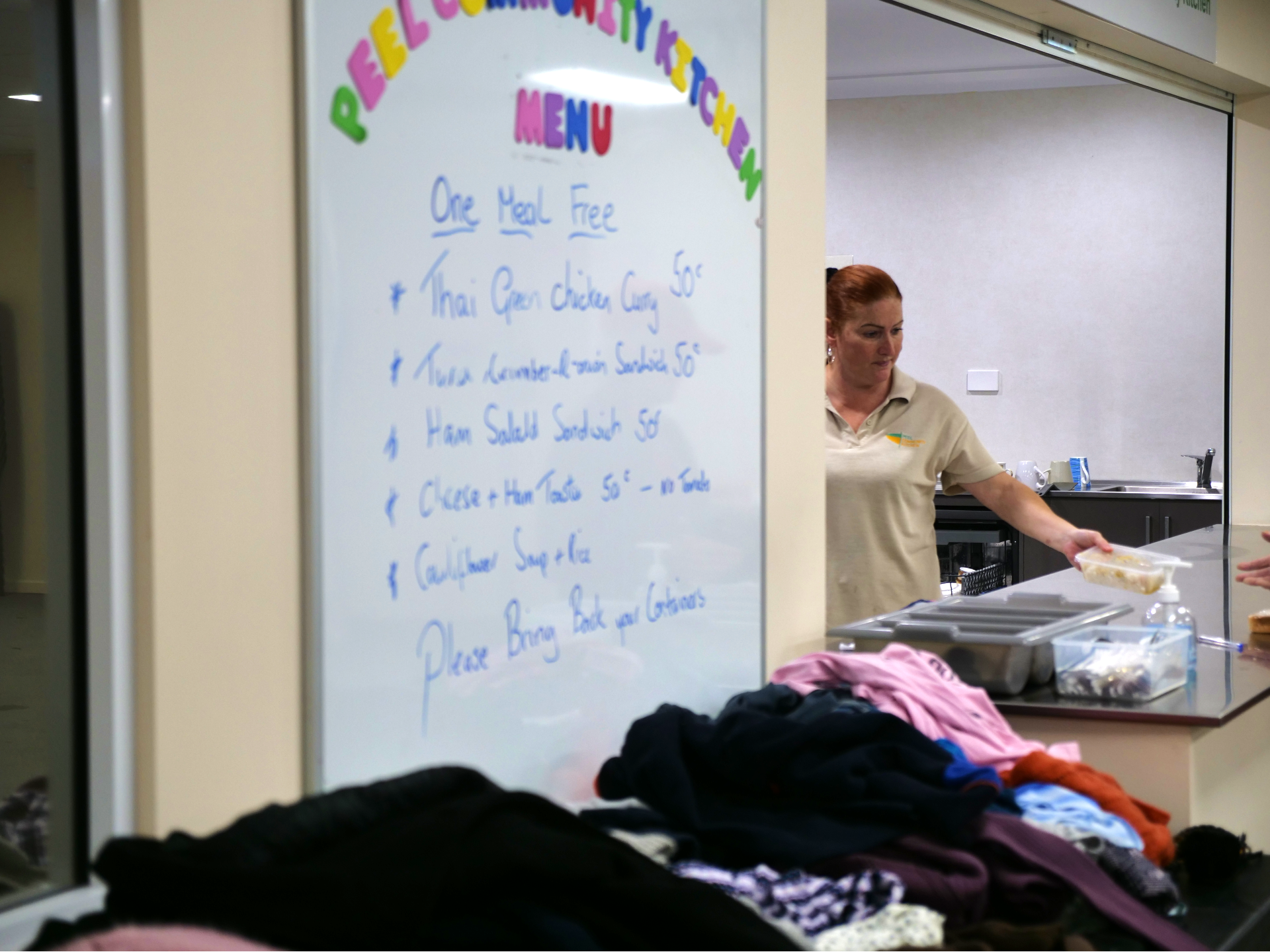A woman hands a hot meal to someone in need at the Peel Community Kitchen