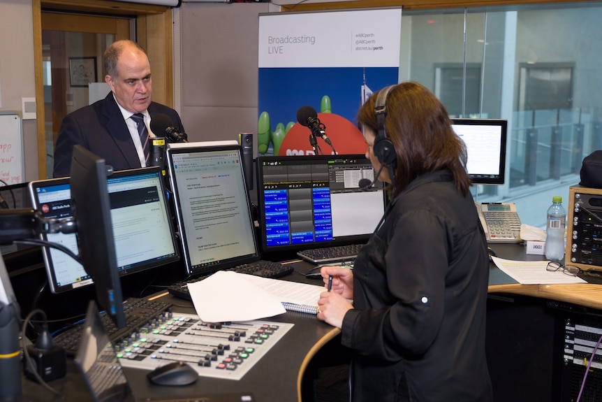 ABC managing director David Anderson stands in a radio studio speaking into a microphone with in Nadia Mitsopoulos opposite him.