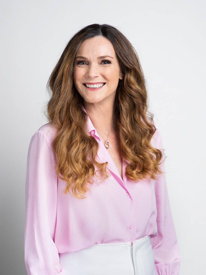 a corporate photo fo a woman in a mauve shirt with long brown hair smiling at the camera