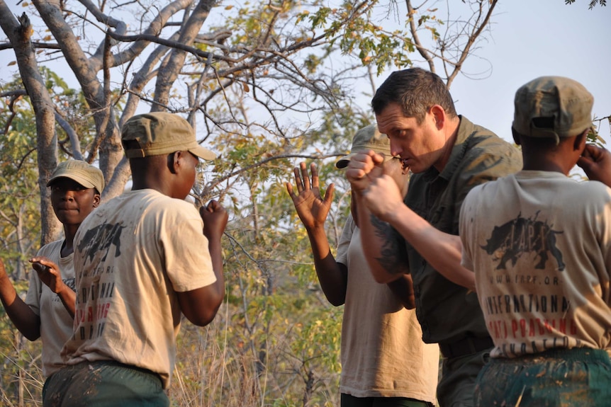 Damien Mander holding up fists, training members of Akashinga rangers, also standing with their fists raised.