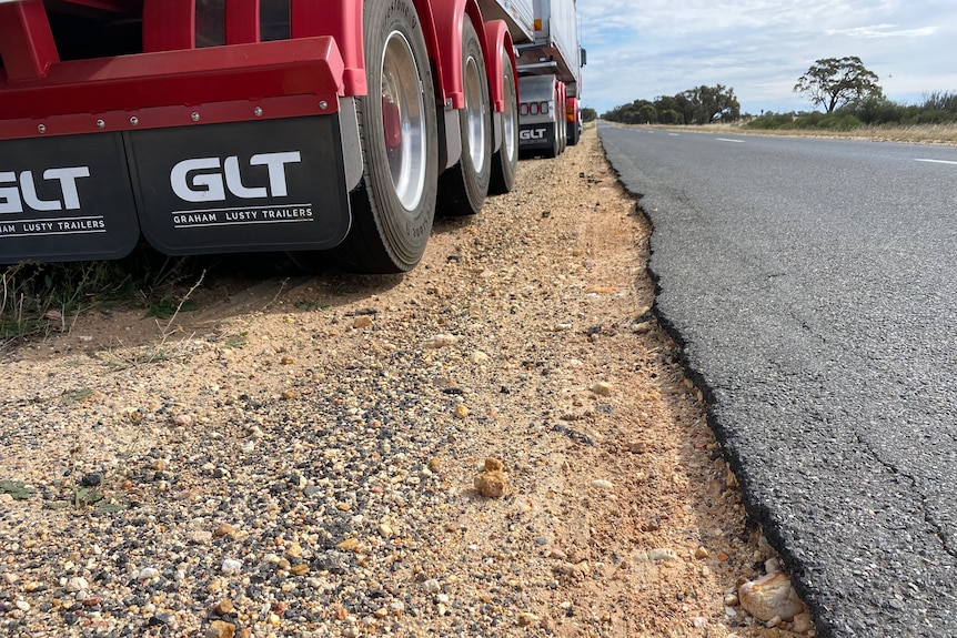 A B-double truck parked on the dirt shoulder of a highway with the bitumen crumbling on the edges.