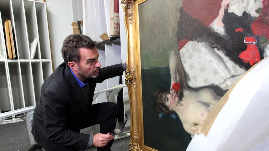 Paul Sumner (left) examines a large painting with part of the cover off with an unnamed staff member.