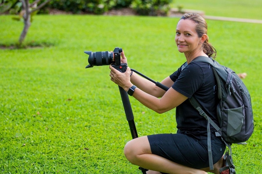 Woman in black kneeling down on grass with a camera on a tripod
