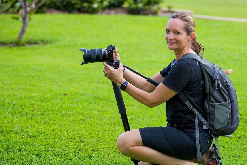 Femme en noir à genoux sur l'herbe avec un appareil photo sur un trépied