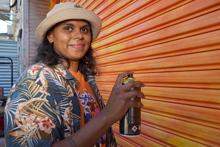 an aboriginal woman wearing a bucket hat and holding a spray can