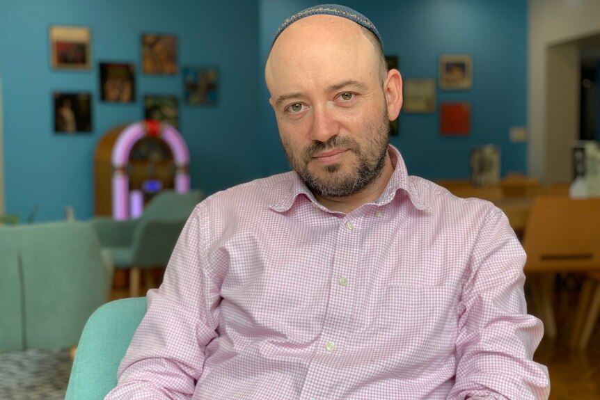 Simon Holloway wearing kippah (skullcap) an sitting in front of blue wall.
