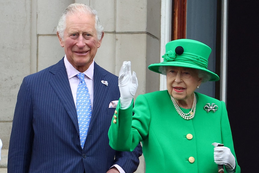 Prince Charles stands next to Queen Elizabeth II, who is waving.