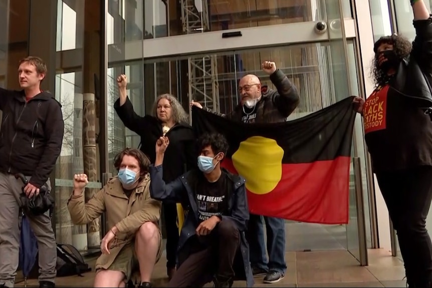 A group of people standing and kneeling outside a court building with their hands in the air.