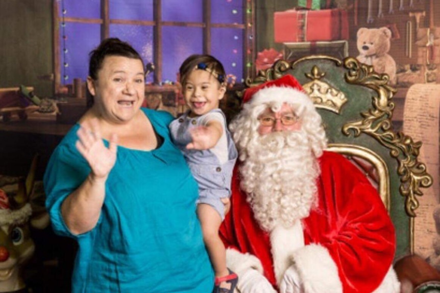 A mum with her toddler son on her hip standing next to a man dressed as Santa 