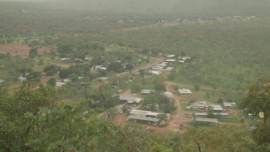 A small town is seen from above, from the vantage point of a lookout. Lush green bush surrounds the buildings. 