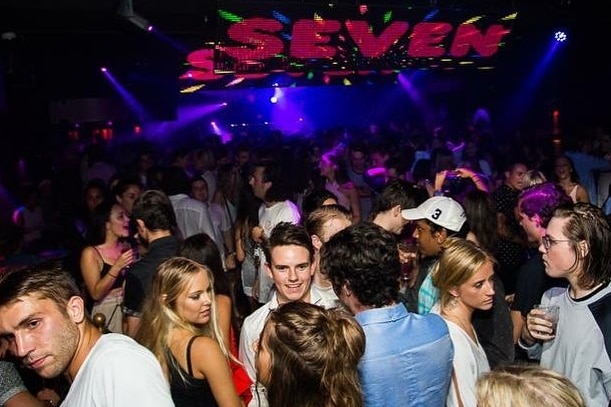 Revellers party in a nightclub under a lightshow displaying the word 'seven'.