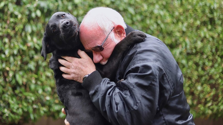 John Hume cuddles a black labrador.