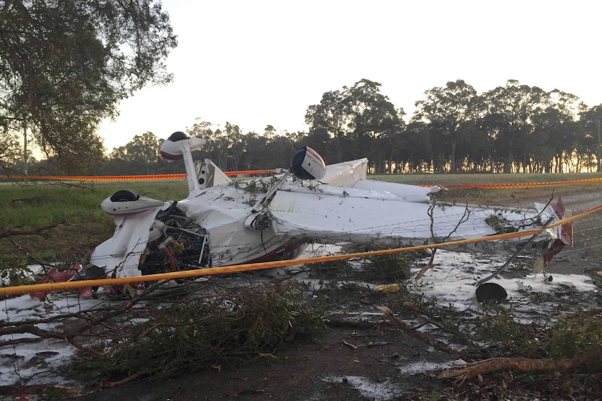 The wreckage of a light plane sits upside down on a dirt road behind police tape.