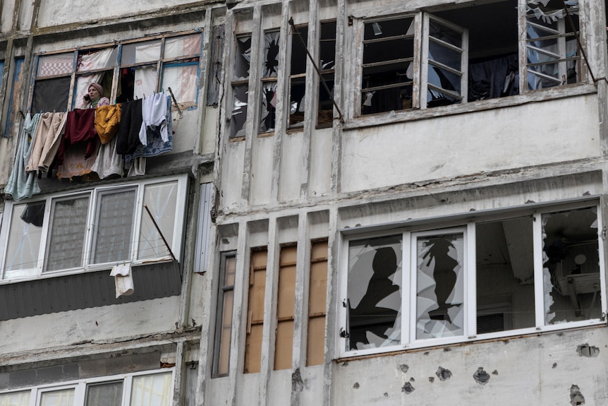 A local woman speaks on her mobile phone in a window of a residential building damaged by a Russian military strike.