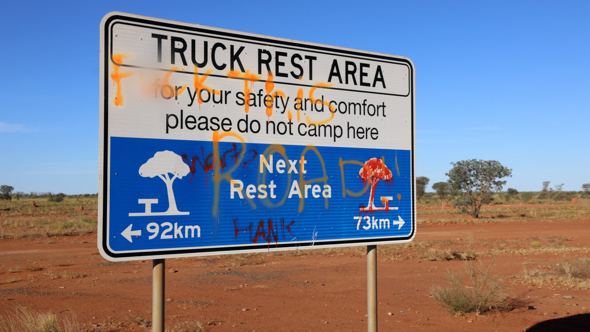 A defaced road sign with red dirt in the background
