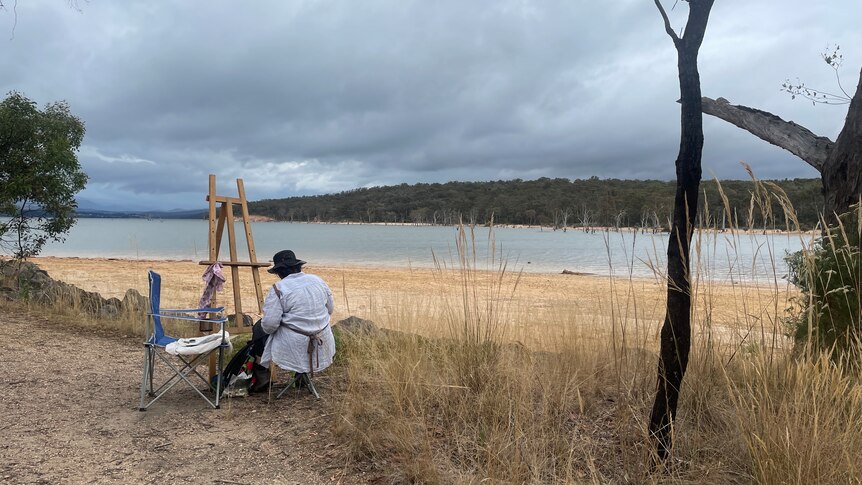 Lone woman painting the lake with easel.
