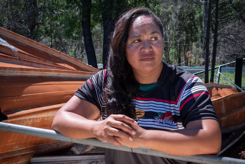 A woman leaning on a railing, with burnt roofing sheets behind her