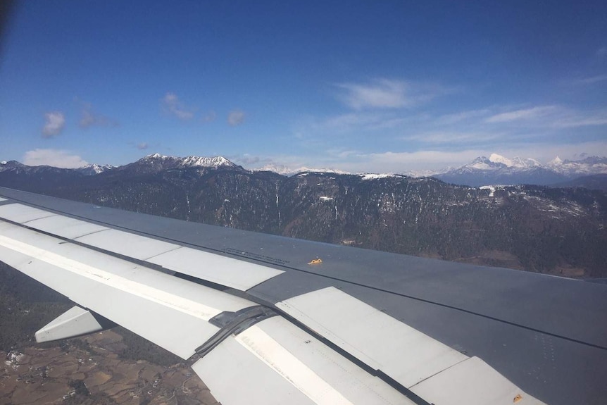 Snow-capped mountains in distance as seen from aeroplane window.