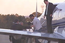 A man in handcuffs steps out from a small plane