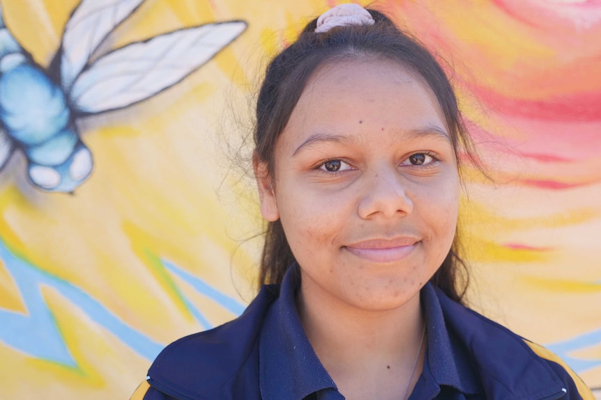 A young Indigenous girl smiles softly looking at the camera.