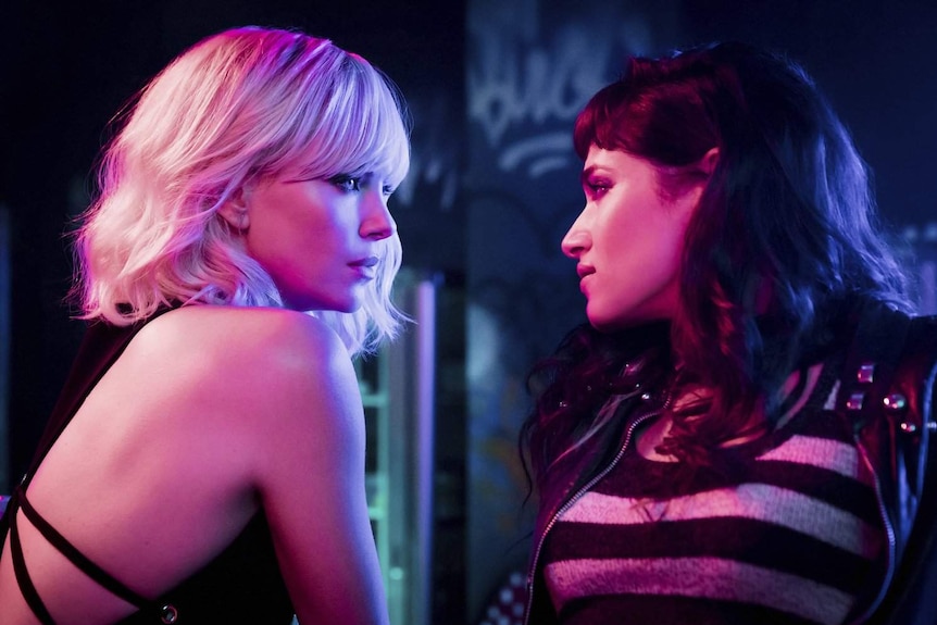 Close-up still image from the film Atomic Blonde featuring Charlize Theron and Sofia Boutella in dark, saturated neon lighting.