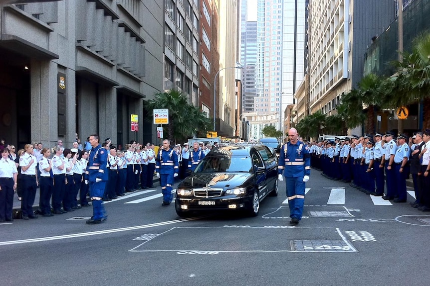 Paramedics walk beside the hearse carrying the coffin of Mike Wilson.