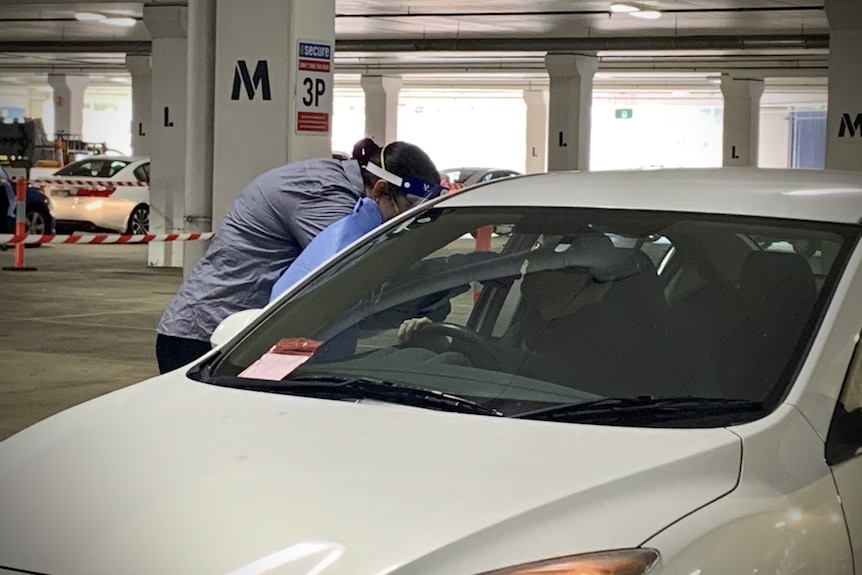 A medical profession tests a man in his car for coronavirus in a Bunnings carpark.