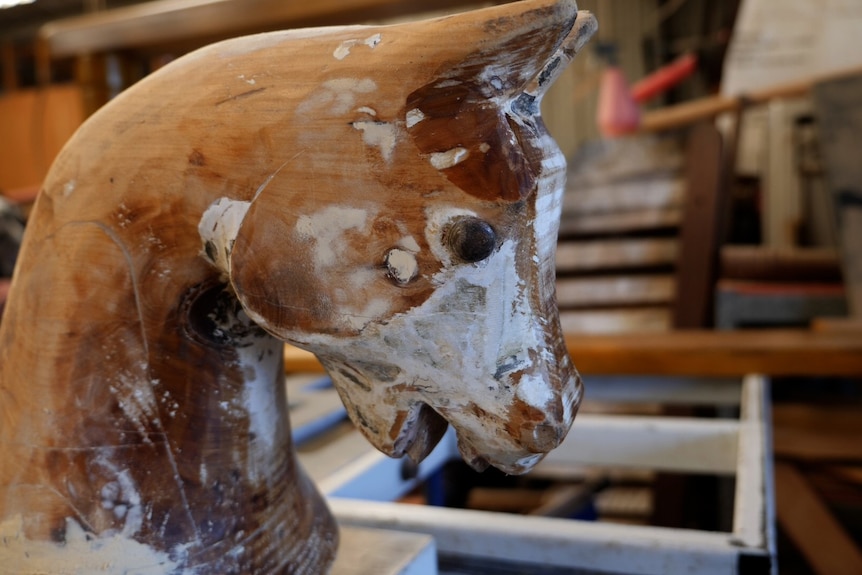 A close up of a wooden toy horse face with white paint scraped back from the face to reveal brown wood