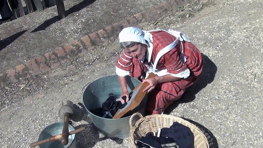 Elderly woman washes clothes in tub with washboard
