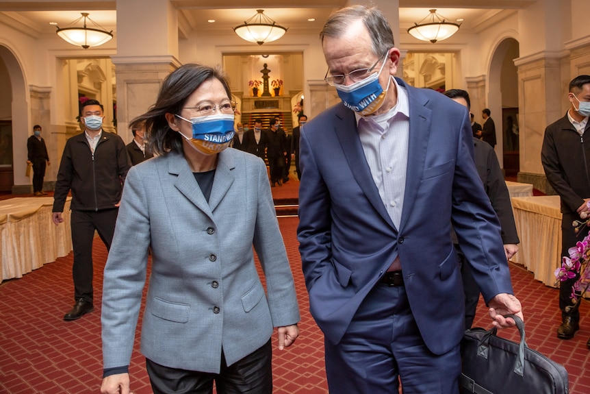 Tsai Ing-wen, in a grey suit, walks next to Mike Mullen. Both are wearing blue and yellow face masks that say STAND WITH UKRAINE