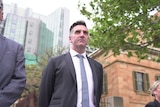 Fraser Ellis stares ahead with his hands behind his back, court buildings are in the background