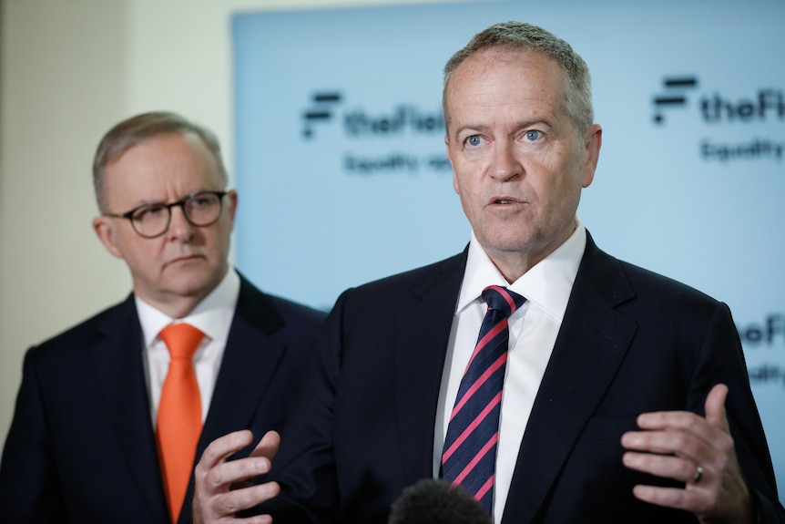 Bill Shorten gestures while speaking at a press conference while Anthony Albanese looks on