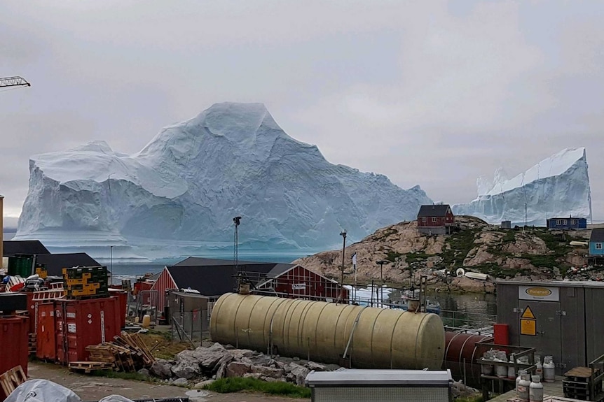 A storage tank is seen as an iceberg floats near the Innaarsuit settlement.