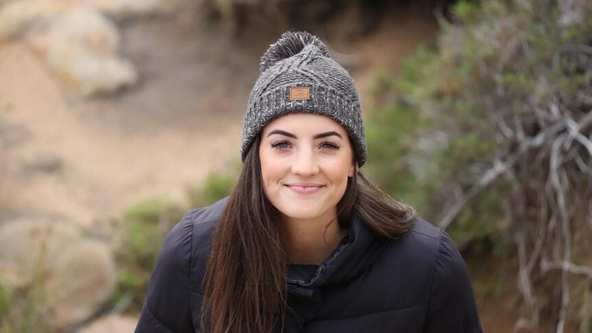 A young woman with long dark hair and a beanie is smiling for the photo