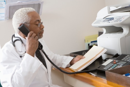 A man in a white coat uses a fax