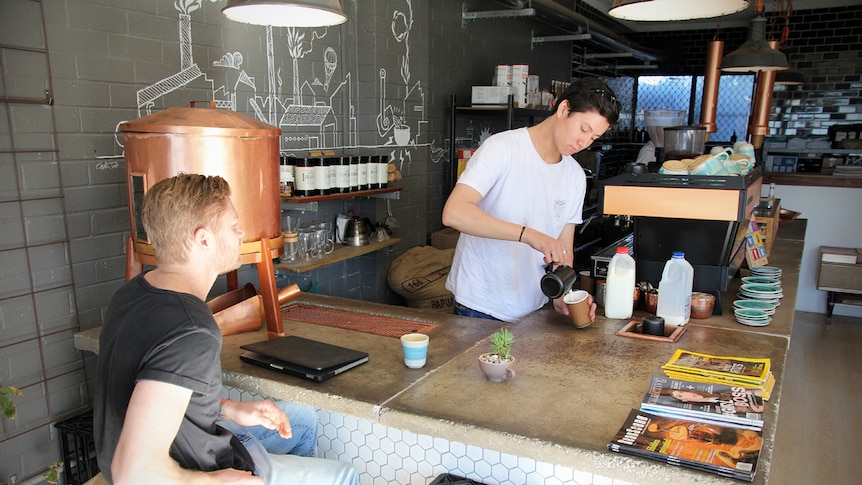 Jayden Martin pours a coffee while Duanne Truter looks on inside a Port Kembla cafe.