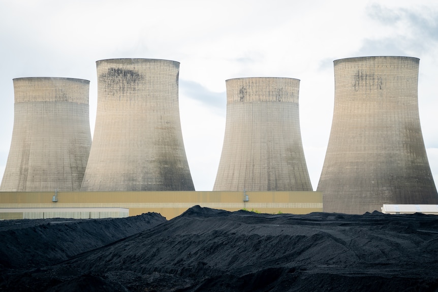 A bed of coal sits in front of cooling towers at a UK powerplant.