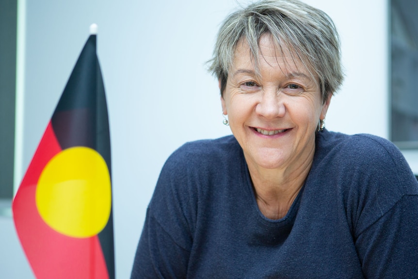 A woman sitting at a desk with a small Aboriginal flag on it.