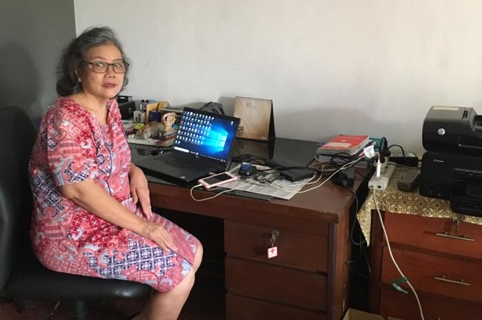 Yanti sitting at desk with laptop on it looking at camera.