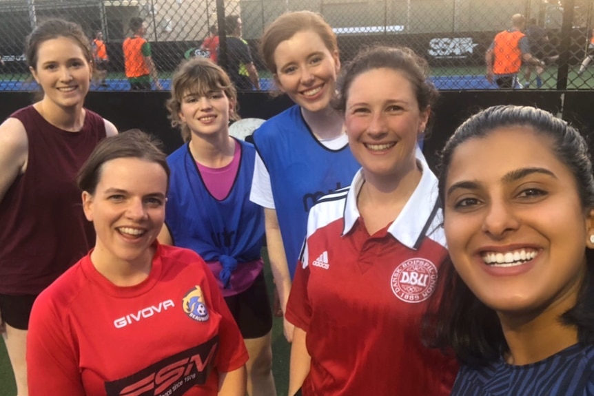 Aish Ravi takes a selfie with women futsal players in the background.