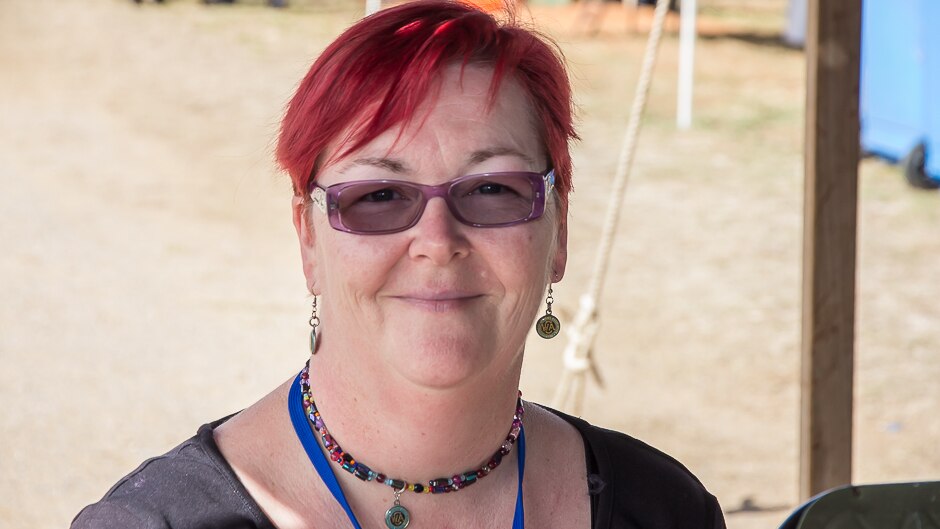 A close up head shot of a woman with red-pink hair and CWA earrings