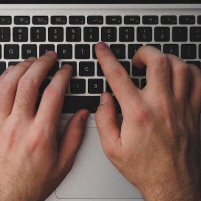 Two hands type on the keyboard of an Apple laptop.